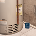 Water heater with a water alarm device on the floor next to it.
